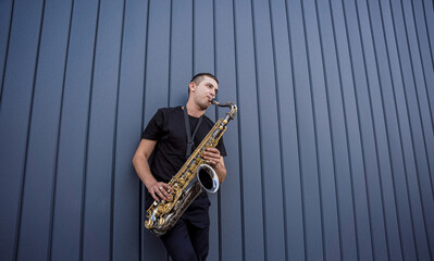 Young street musician playing saxophone near the big blue wall