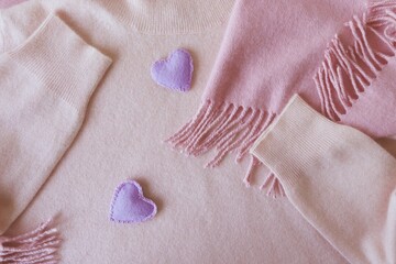 Lilac felt hearts adorn pink cashmere clothes, top view, valentine day concept, warm cozy products