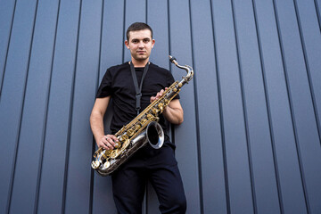 Young street musician playing saxophone near the big blue wall