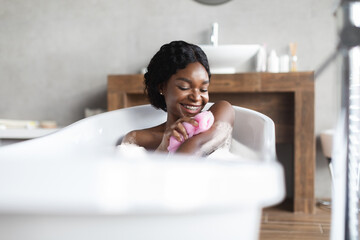 Happy young black lady taking foamy bath, exfoliating skin