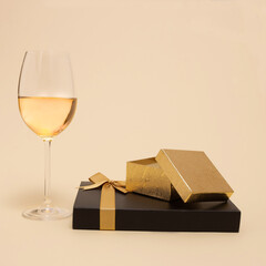 Black and golden gift boxes beside a glass of white wine on pastel beige background. Christmas and New Year composition. Minimal holiday concept.