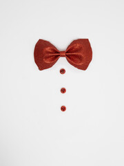Red bowtie with red buttons on white background.  Christmas suit composition with decoration. New Year Flat lay. Top view.