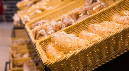 fresh golden breads with melted cheese wrapped in plastic wrap in wicker basket in bread department of supermarket