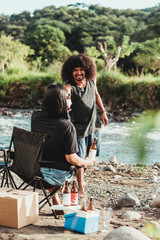 un hombre latino sonriente recibiendo una cerveza de una mujer sentada en una silla a la orilla de un río disfrutando del verano de Costa Rica