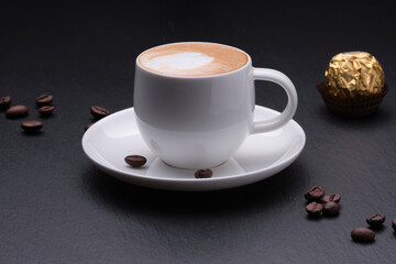 Coffee with milk, candy, black background close. White cup of coffee with coffee beans on a black background side view.