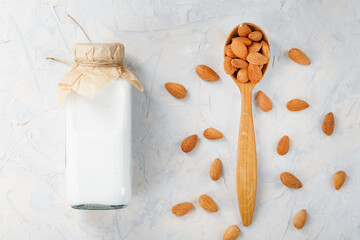 Fototapeta na wymiar Almond milk in a glass bottle on a light background with a scattering of seed kernels and a wooden spoon.