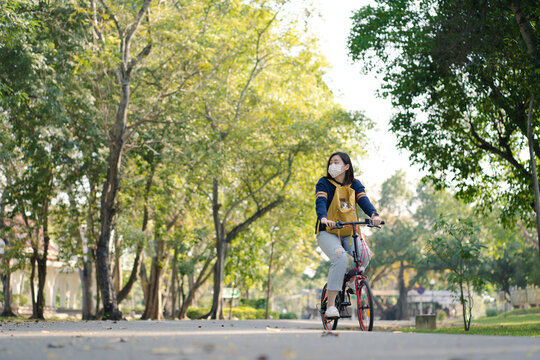 Asian Woman Wearing Facemask And Biking Bicycle With Her Cat In Backpack At Park