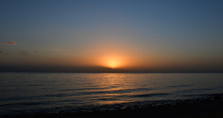 The sun rises over the sea from behind the mountains. ripples on the surface of the water. Dawn in dark colors