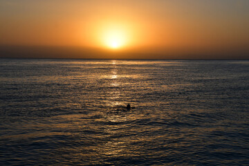 Sunrise over the sea. The bright yellow-gold color of the sky. The glare of the sun and a slight swell on the surface of the water