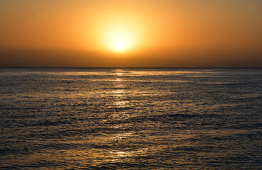 Obraz premium Sunrise over the sea. The bright yellow-gold color of the sky. The glare of the sun and a slight swell on the surface of the water