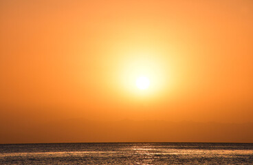 Sunrise over the sea. The bright yellow-gold color of the sky. The glare of the sun and a slight swell on the surface of the water