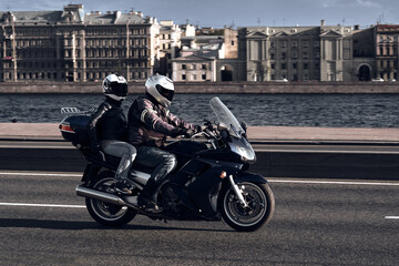 Fototapeta na wymiar A man and a woman ride together on a sports motorcycle along the embankment. Motorcyclists drive around the city in the evening on a dark blue sports bike.