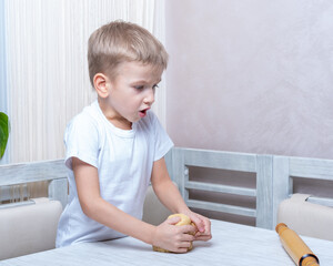 Fototapeta premium Cooking traditional gingerbread. Emotional boy kneads raw dough to make cookies. Child helps mom with Christmas cooking