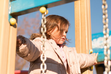 Obraz premium Small child with long red hair against the background of a blue sky in warm clothes on the playground