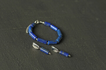 Blue natural lapis lazuli Bracelet, earrings made of natural stones lies on black modern concrete background. Blue stone lapis lazuli. Handmade jewelry bracelets, earrings from natural stones