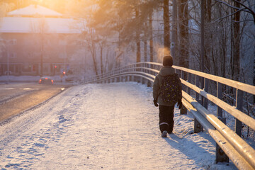 School child waling on a street with a backpack during snowy winter day