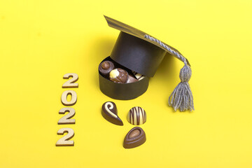 A box of chocolates in the form of a graduation hat. Chocolate day concept. Graduation 2022 on yellow background copy space