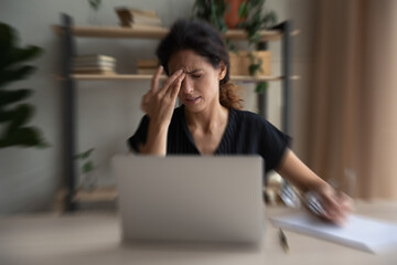 Unhealthy Hispanic woman work on laptop at home office struggle with blurry vision or dizziness....