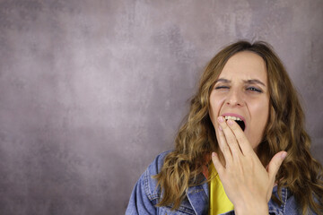 young girl yawns, dressed in casual clothes on a gray background