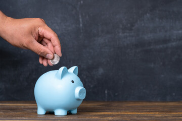 A man's hand puts a coin into a blue piggy bank. Copy space