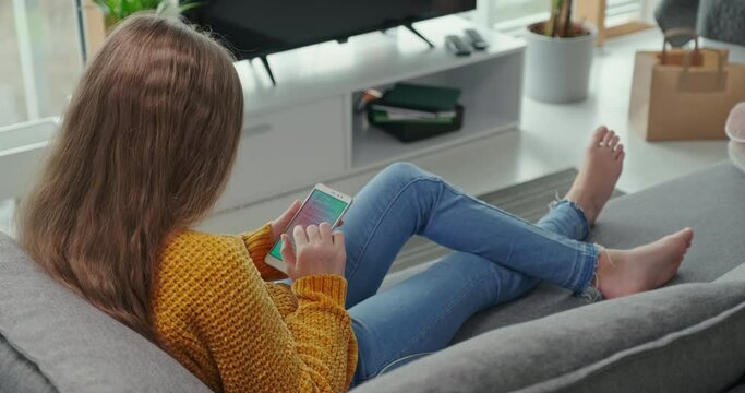 Portrait preteen girl using mobile phone and relaxing on the couch. She is online