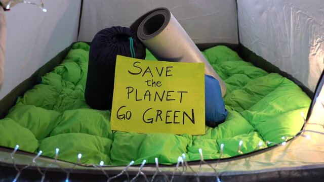 Italy, Milan , Activist man 40 years old with sign Save the Planet , go green - Friday for Future Youth 4 Climate - boy camping home in tent during Covid-19 Coronavirus lockdown - no planet B