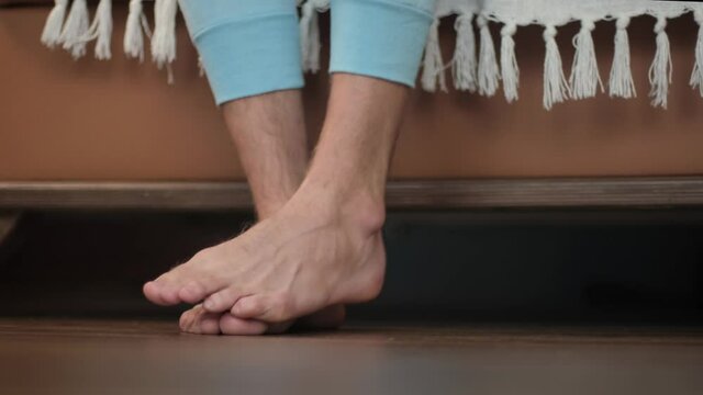 Male feet getting out of bed touching barefoot cold floor, close-up