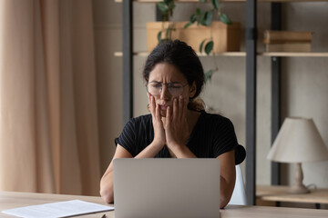 Sad young Hispanic woman look at screen work online on computer at home office feel unmotivated bored. Unhappy Latino female distressed with bad negative news or message on laptop on internet.