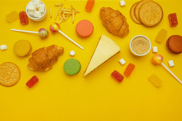 French croissant, candy on a stick, jelly candies, marshmallows, cookies and macarons on a yellow bright background. Unhealthy foods on a colored background, top view.