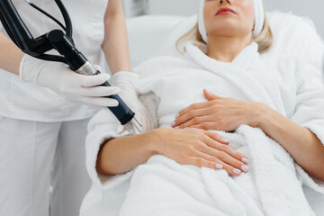 Fototapeta premium A young girl gets carbon peeling for the skin of her hands in a beauty salon. Laser pulses cleanse the skin. Hardware cosmetology. The process of photothermolysis, warming the skin.