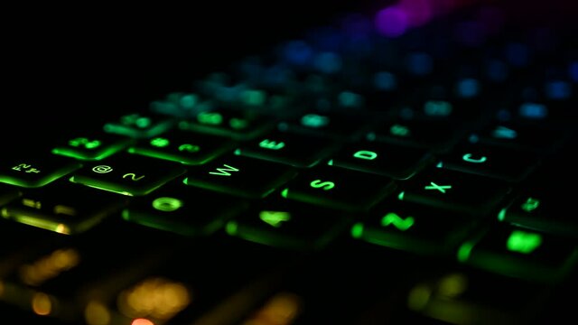 Keyboard with RGB backlit illumination changing colors for virtual video games and editing on powerful Computer in dark office room. Rainbow spectrum in modern technology.