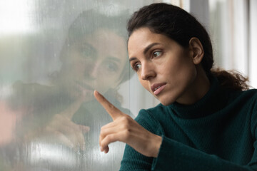 Upset young Latino woman look in window distance feel depressed unhappy alone at home. Sad stressed...