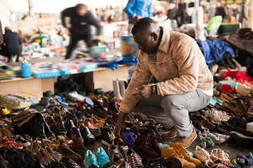 Obraz premium Afro-American guy considers sacond hands shoes on flea market