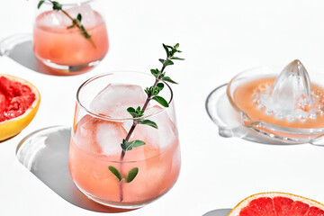 Summer grapefruit cocktail. Fresh healthy grapefruit beverage with herbs on sunlight with hard shadows. Creative drink with palm leaf on light blue pastel background.