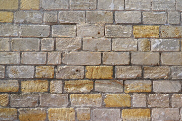 An old wall of gray, white and yellow rectangular blocks and bricks with traces of saw cuts and chips.