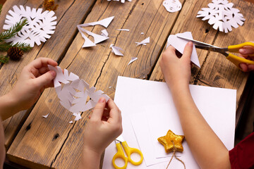 children's hands cut snowflakes from paper at home on a wooden background