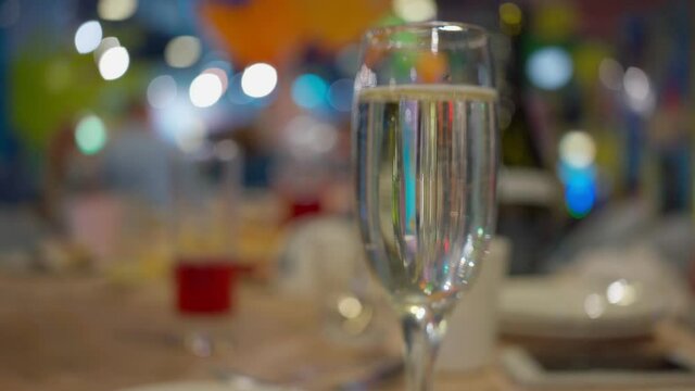 glass of champagne against background bright multicolored festive table. Multi-colored bokeh. Beautiful video with glass of wine on background party table. Place for text copy space. Birthday party
