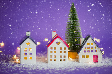 Fototapeta na wymiar Cozy houses and Christmas tree in snowstorm on violet background and fairy lights. Winter, snow - home insulation, protection from cold and bad weather. Festive mood, Christmas, New Year greeting card