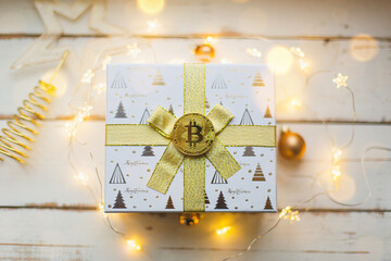 A Bitcoin coin on a box with a gift for Christmas and new year. Cryptocurrency, finance, wealth and investing. Fairy lights, greeting card