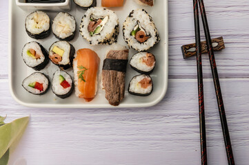 Teilausschnitt von Sushivarianten ordentlich angerichtet auf einen Teller mit Essstäbchen auf weißem Holzuntergrund