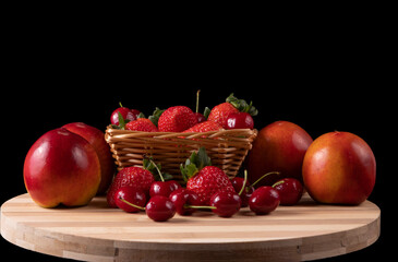 Basket with strawberries and cherries and nectarines. Bamboo board. black background. Space for text.