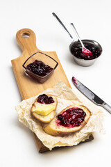 Jam in glass bowl, loaf slices with butter and jam on cutting board.