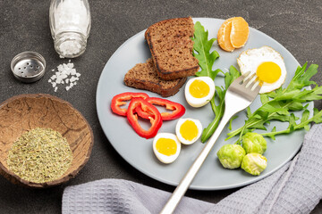 Fork and fried egg, Brussels sprouts, chopped red peppers and half boiled egg on gray plate.