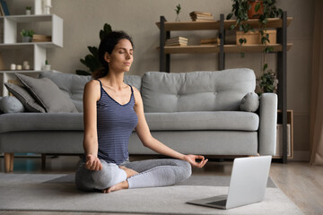 Calm young Hispanic woman meditate with mudra hands watch video online training on computer at home. Healthy peaceful Latino female practice yoga with webcam distant lesson or session on laptop.