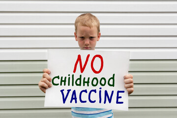 Angry little boy holding poster with message No childhood vaccine. Anti-vaccination and protection...