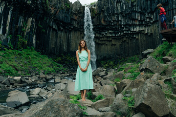 beautiful girl in a dress next to Svartifoss waterfall in the Skaftafell National Park, iceland