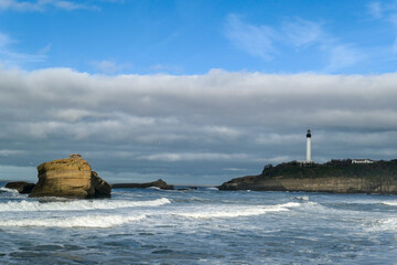 Praia em Biarritz com formações rochosas e um farol ao fundo