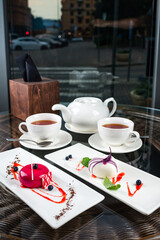 Two Small French ball shaped cakes mousse dome served on a plate with cups of tea