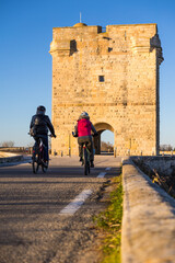 Cyclistes devant la Tour Carbonnière au milieu des marais de la Petite Camargue, près d’Aigues-Mortes (Occitanie, France) - obrazy, fototapety, plakaty