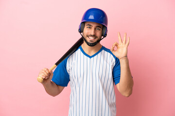 Baseball player with helmet and bat isolated on pink background showing ok sign with fingers